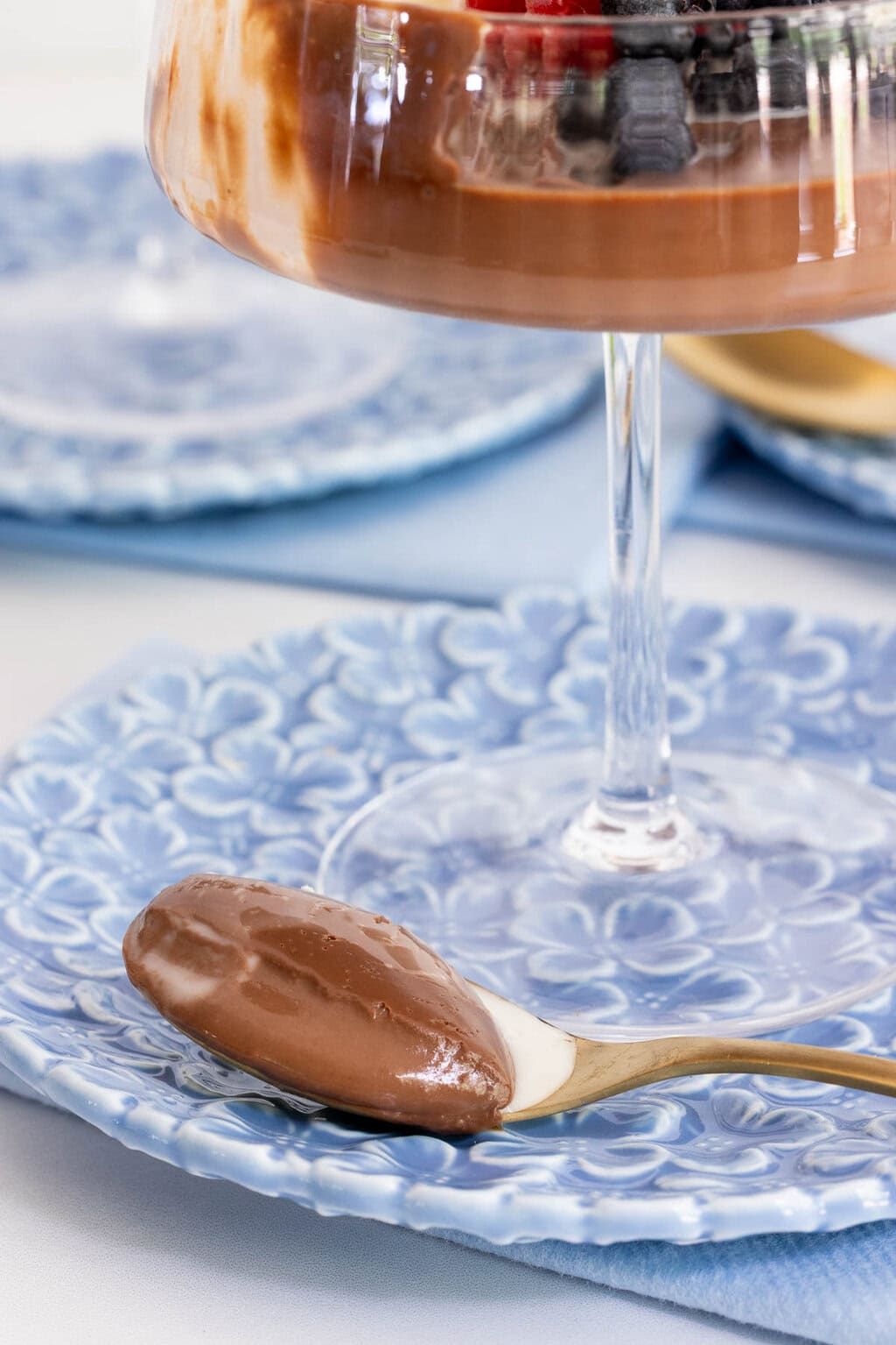 Close-up of a spoonful of chocolate panna cotta showing its smooth, creamy texture beside a glass dessert coupe.