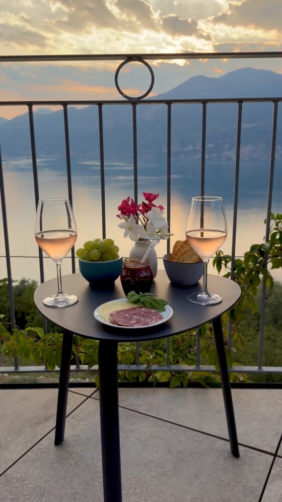 A sunset aperitivo with rosé, local cheeses, salami, grapes, and flowers on a balcony overlooking Lake Garda.