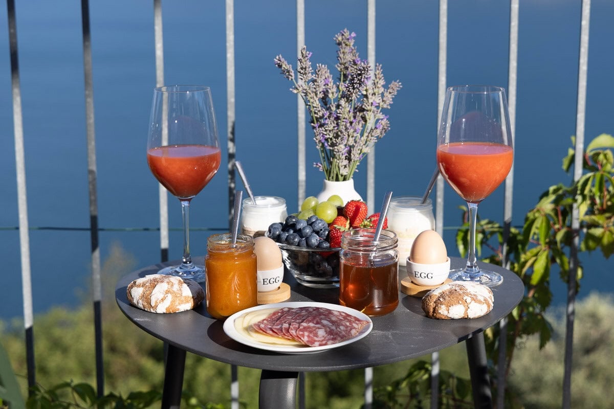 Breakfast table on a Lake Garda terrace with fresh fruit, homemade jams, farm eggs, local meats, and panoramic lake views.