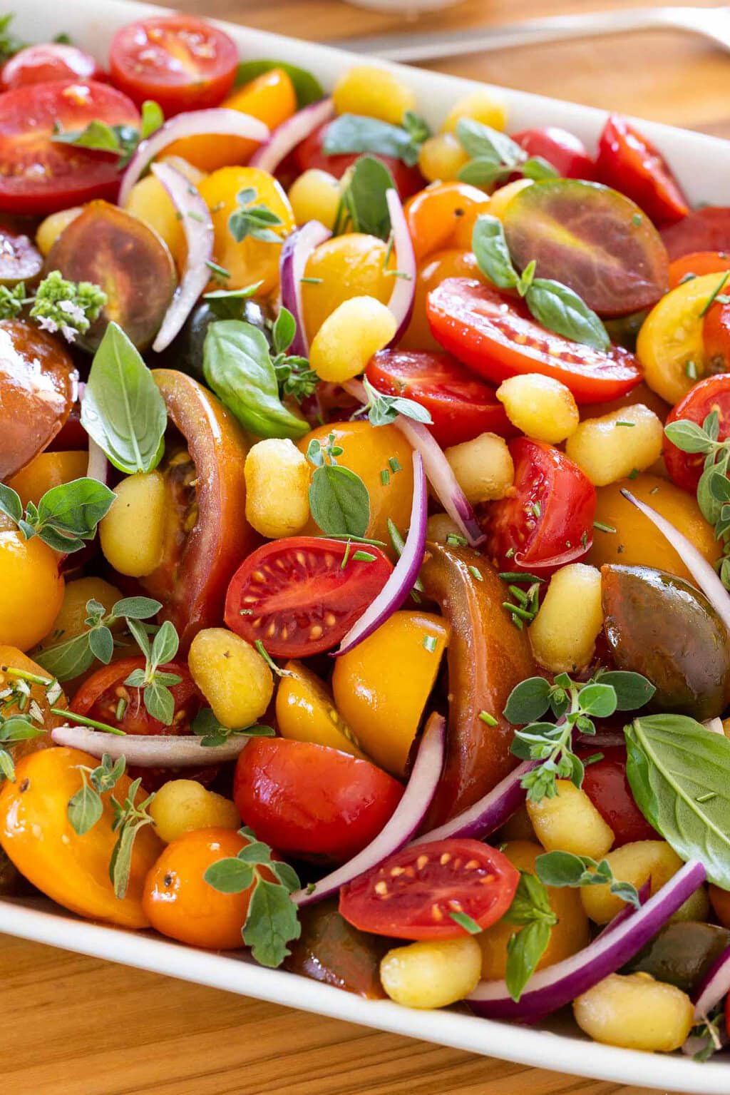 Close-up of crispy gnocchi salad with colorful heirloom tomatoes, cherry tomatoes, fresh basil, oregano, red onion, and crispy golden gnocchi.