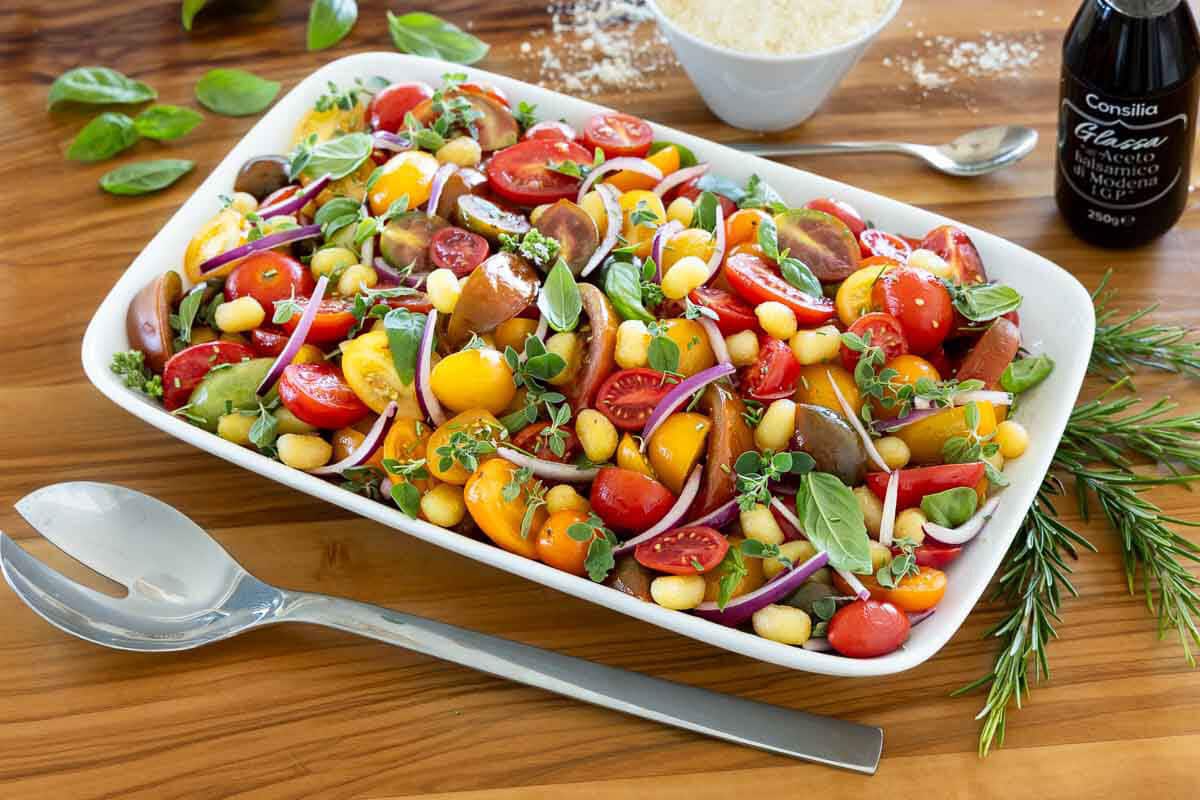 Serving platter of crispy gnocchi salad with heirloom tomatoes, cherry tomatoes, fresh basil, herbs, red onion, Parmesan, and balsamic glaze.