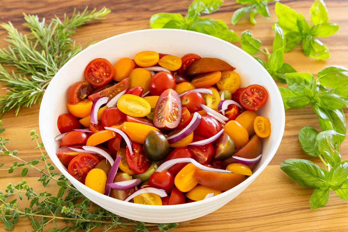 Bowl of colorful heirloom and cherry tomatoes with sliced red onion prepared for crispy gnocchi salad.