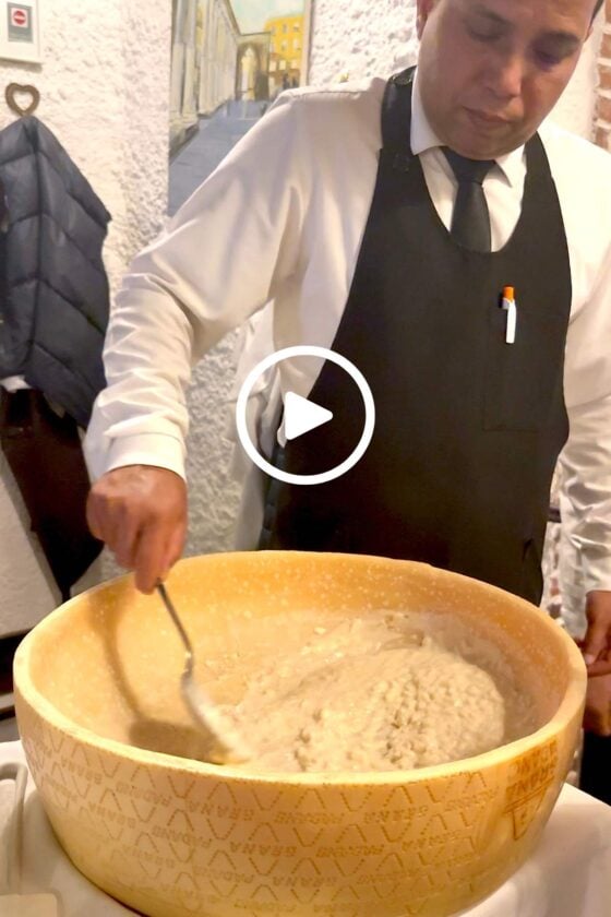 A restaurant server stirring creamy risotto inside a giant Parmesan cheese wheel during a tableside presentation in Milan, Italy.
