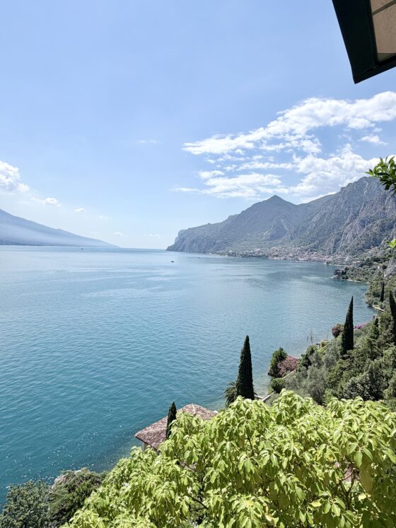 Panoramic view of Lake Garda with crystal-clear blue water, dramatic mountains, and lush greenery along the shoreline in northern Italy.