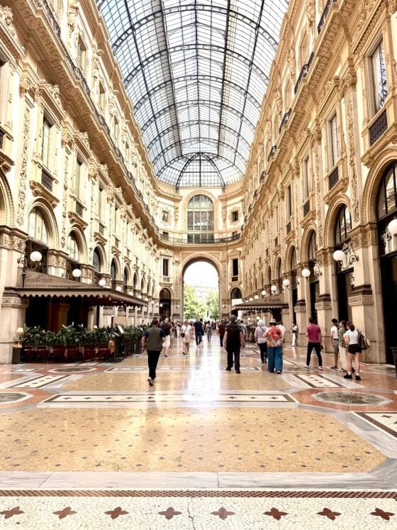 Interior of the historic Galleria Vittorio Emanuele II in Milan, Italy, featuring its soaring glass ceiling, ornate architecture, mosaic floors, and elegant shops.