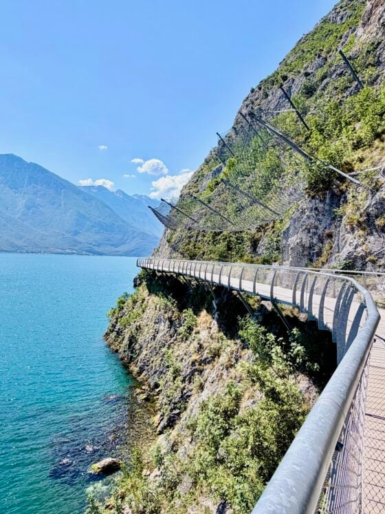Cliffside cycling path overlooking the blue waters of Lake Garda with dramatic mountain scenery in northern Italy.