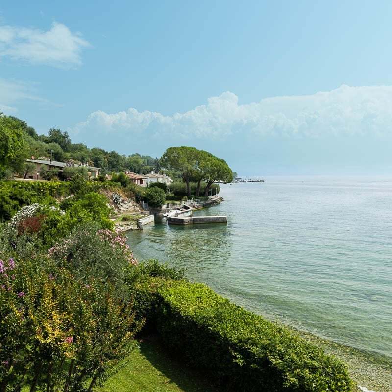 Scenic view of Lake Garda's crystal-clear water, lush shoreline, and colorful gardens in northern Italy.