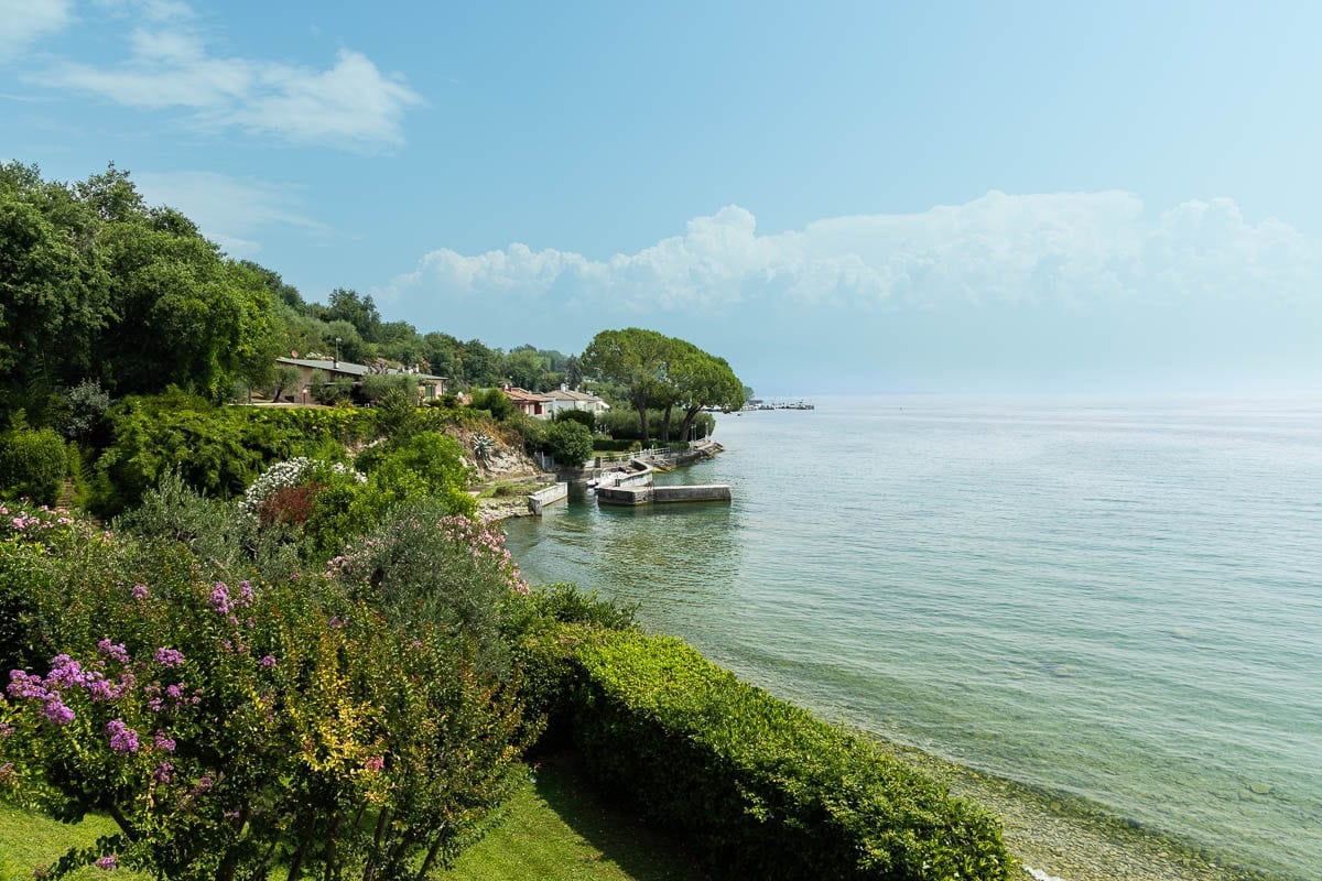 Scenic view of Lake Garda's crystal-clear water, lush shoreline, and colorful gardens in northern Italy.