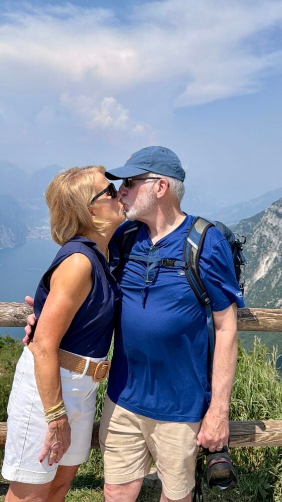 Chris and Scott sharing a kiss on Monte Baldo while celebrating their 50th wedding anniversary with panoramic views of Lake Garda, Italy.