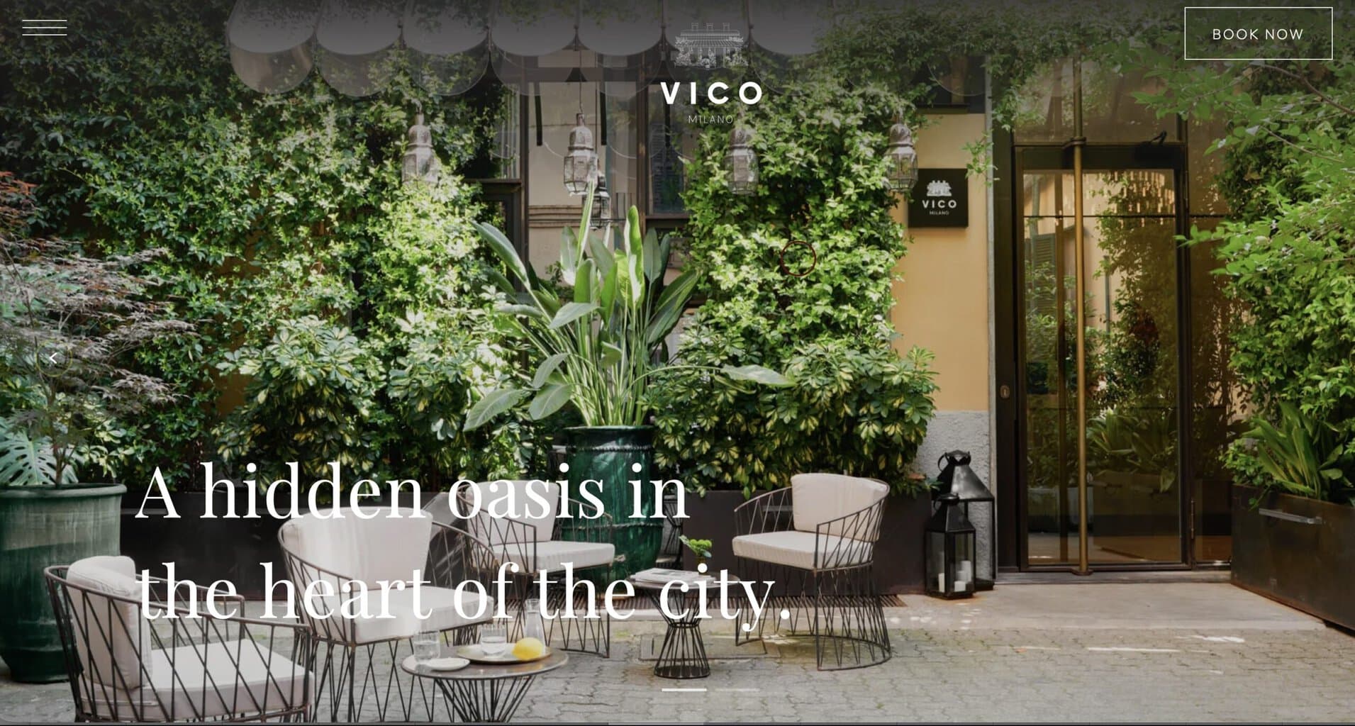 Courtyard entrance to Vico Milano boutique hotel/restaurant with lush greenery and outdoor seating in Milan, Italy.