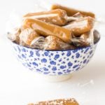 Vertical photo of 8 Minute Microwave Salted Caramels wrapped in plastic in a blue and white bowl.