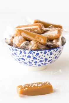 Vertical photo of 8 Minute Microwave Salted Caramels wrapped in plastic in a blue and white bowl.