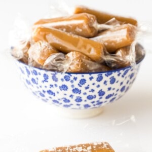 Vertical photo of 8 Minute Microwave Salted Caramels wrapped in plastic in a blue and white bowl.