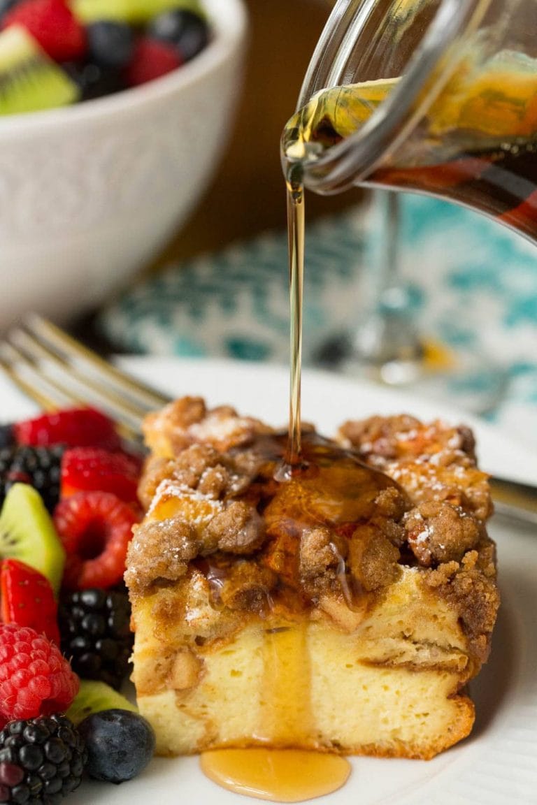 Vertical picture of overnight french toast cut into a square with fresh fruit with syrup poured on top
