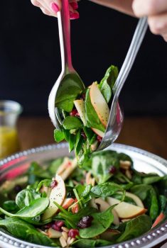 Vertical picture of Apple Cranberry Spinach Salad in a silver bowl with salad tongs