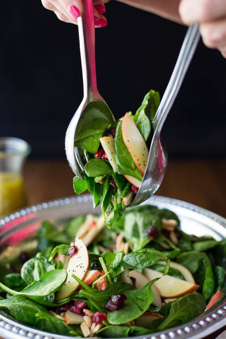 One of 15 Delicious Fall Salads - Overhead photo of a person tossing an Apple Cranberry Spinach Salad in a pewter serving dish.