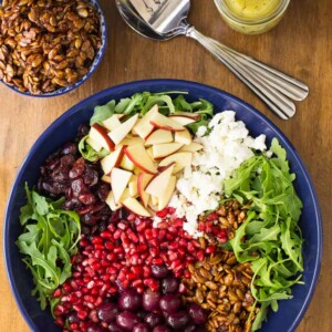 Vertical overhead picture of Arugula Roasted Grape Salad with ingredients separated into sections in the bowl