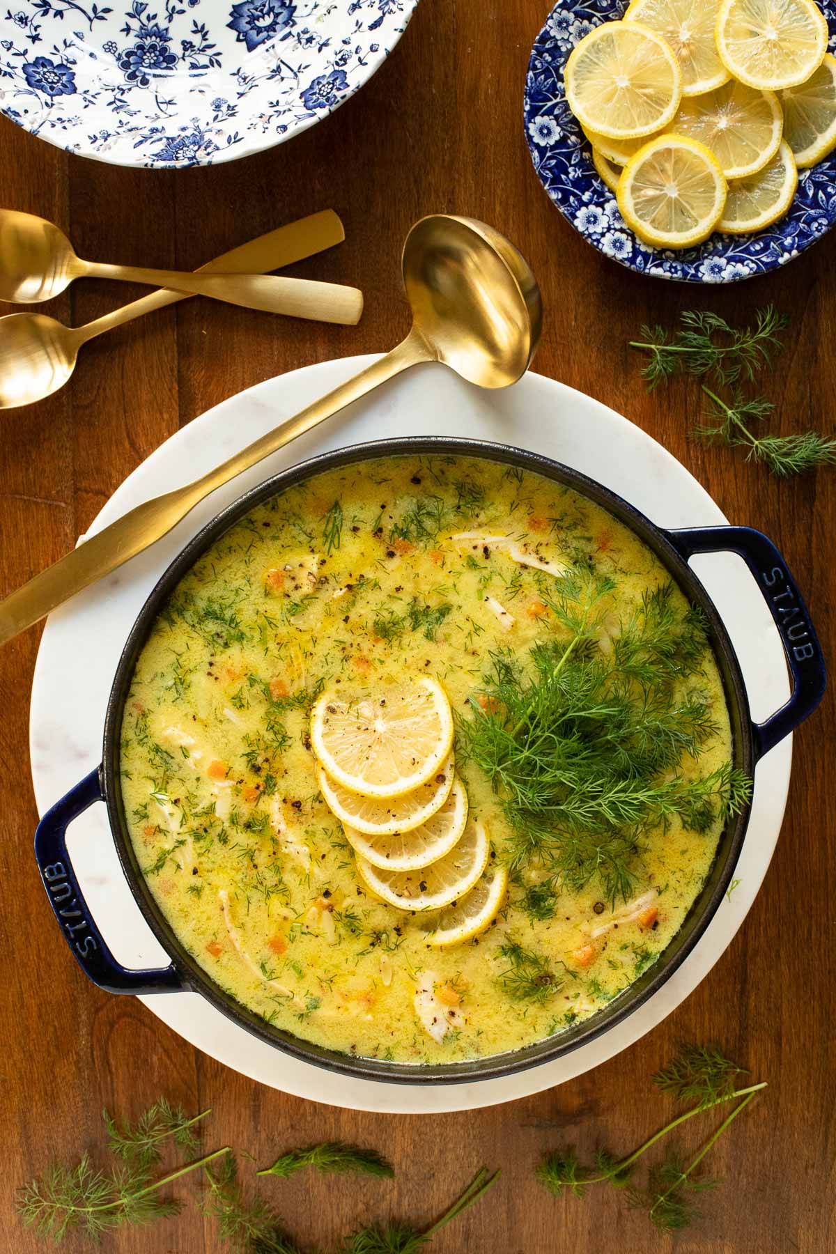 Overhead vertical photo of Avgolemono in a deep blue Staub cast iron pot garnished with lemons and fennel.