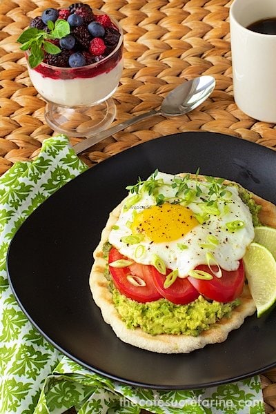 Photo of a plate of Avocado Breakfast Flatbreads on a wicker table with a green and white napkin underneath the plate.