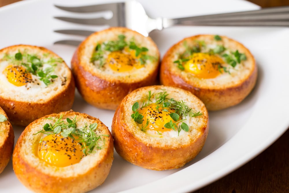 Closeup photo of a white serving platter filled with Baked Eggs in Bread Baskets.