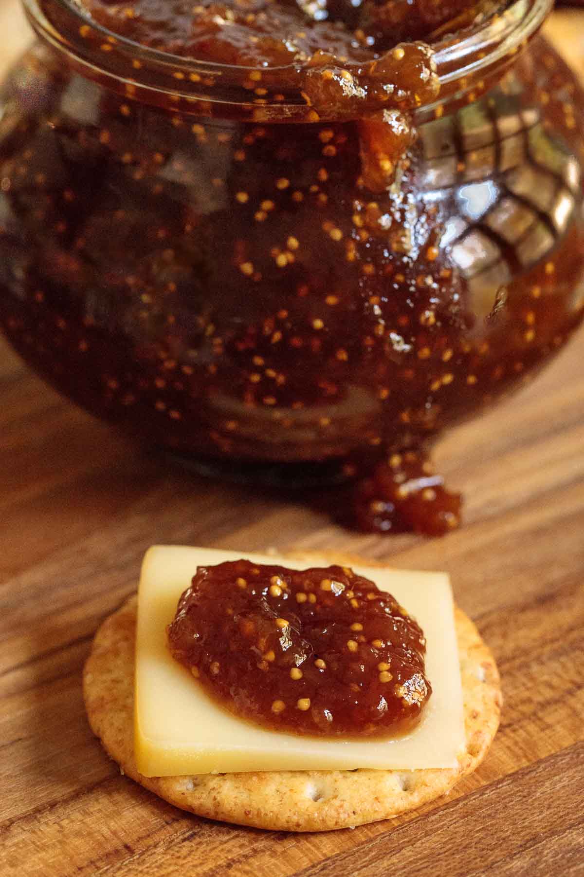Photo of a jar of Easy Balsamic Fig Jam and a cracker with cheese and the jam in the foreground.