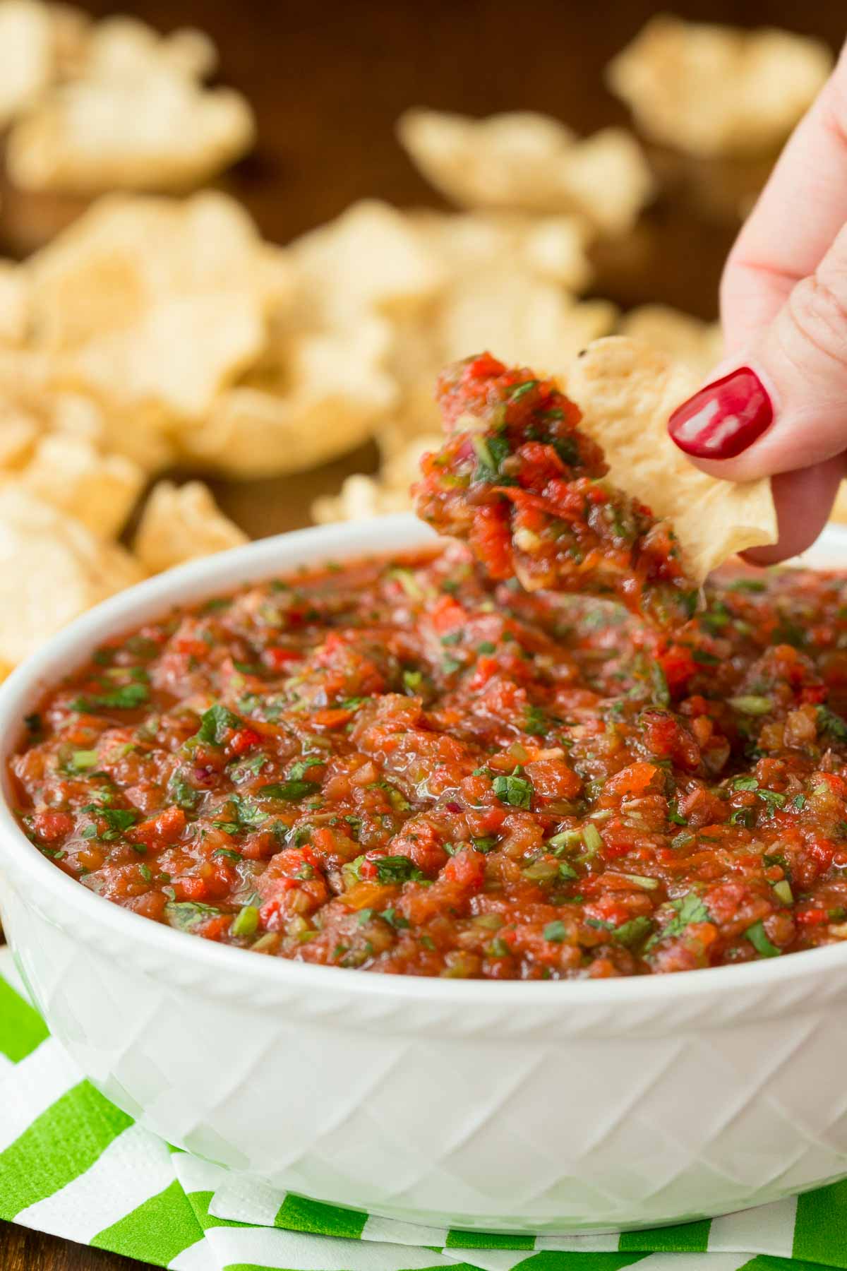 Vertical photo of Easy Fresh Salsa in a white bowl on a green and white striped napkin with tortilla chips in the background.