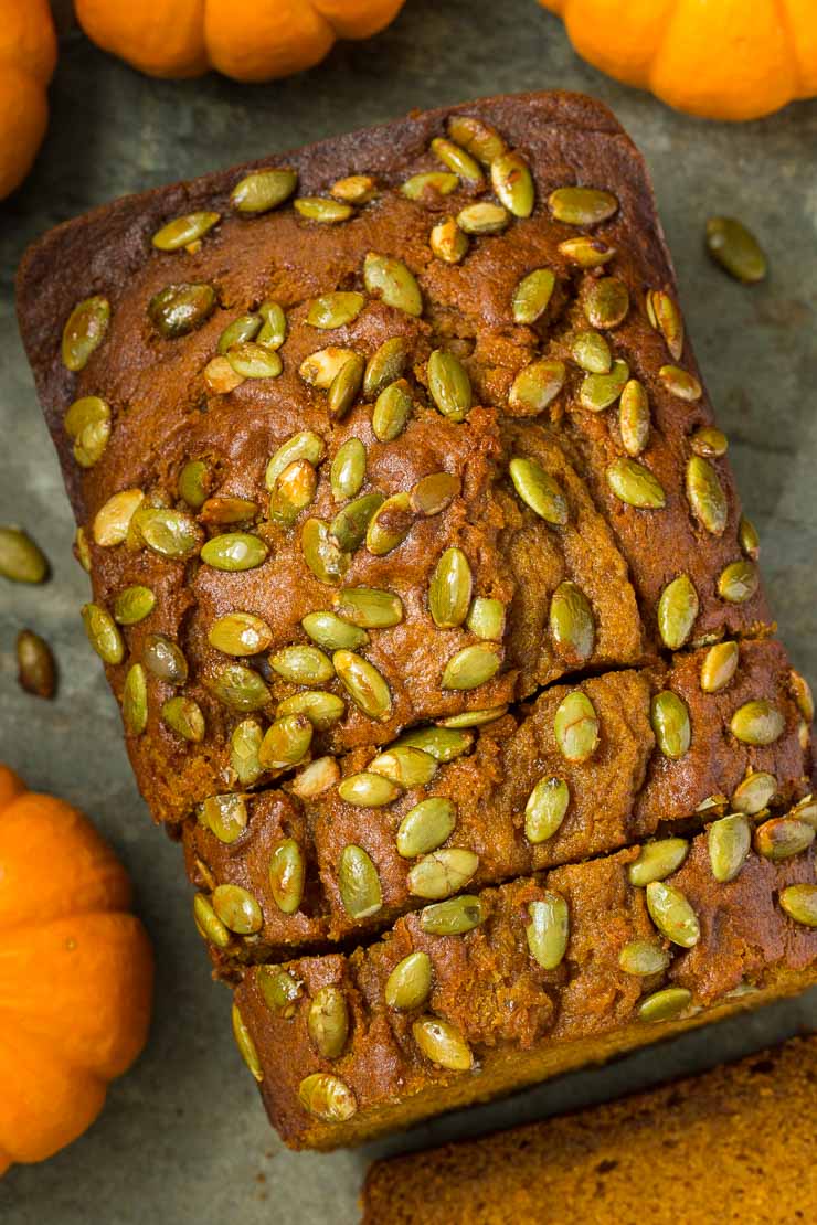 Overhead closeup photo of a loaf of Better Than Starbucks Pumpkin Bread sliced and surrounded by miniature pumpkins.