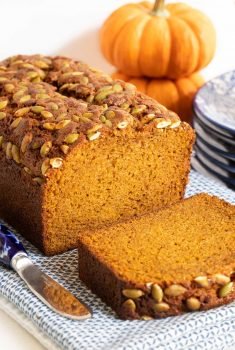 Vertical photo of the front of a loaf of Better Than Starbucks Pumpkin Bread with a slice cut in the front surrounded by mini pumpkins.