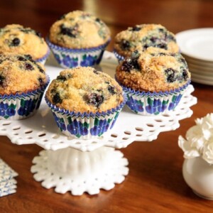 Horizontal closeup photo of a batch of Better than Starbucks Blueberry Muffins on a white lattice pedestal serving plate.