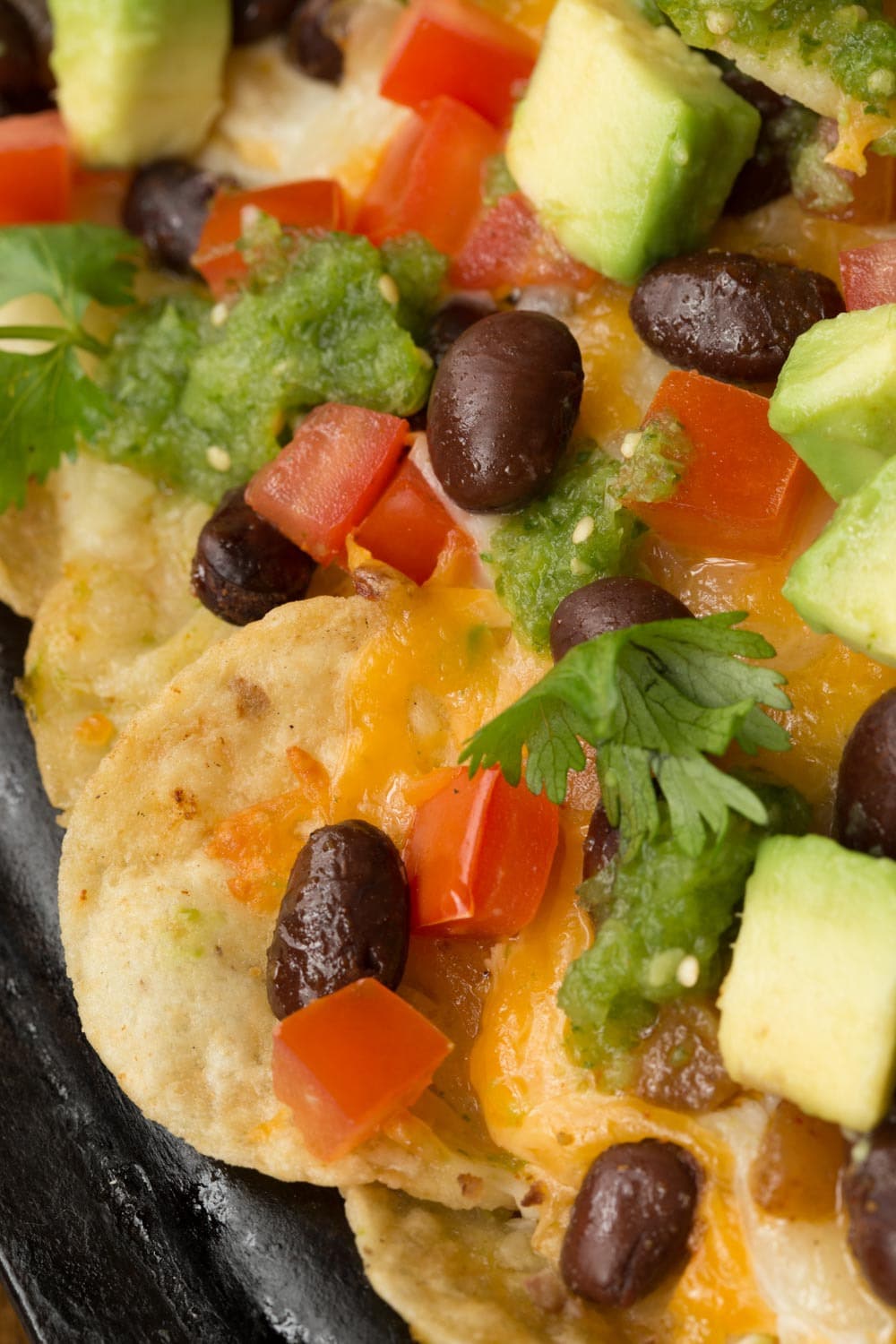 Extreme closeup overhead photo of Black Bean Nachos with Salsa Verde garnished with cilantro and sliced avocados.
