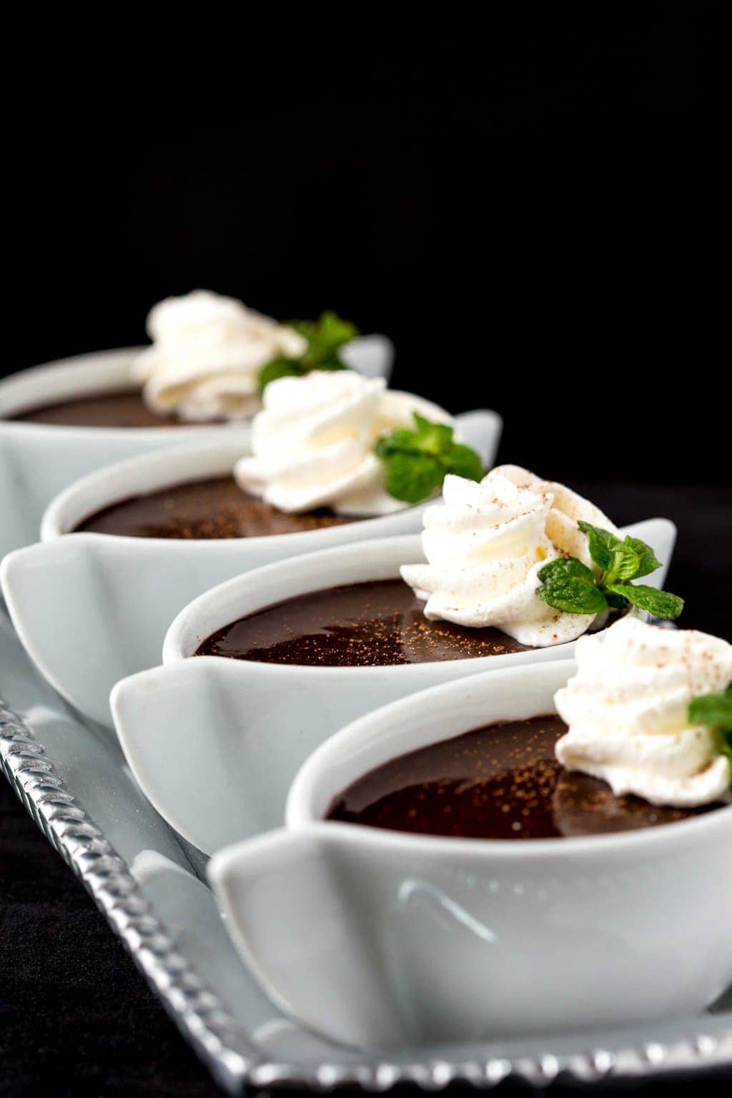 Vertical closeup photo of Blender Chocolate Pots de Crème in small white dessert dishes garnished with whipped cream and a sprig of fresh mint.