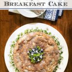 Overhead vertical photo of a Blueberry Buttermilk Breakfast Cake on a white serving plate on a wood table.