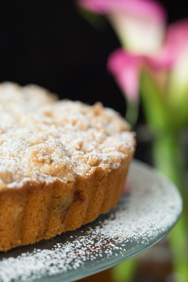 Vertical Image of Blueberry Crumb Cake with pink calla lilies in the background.