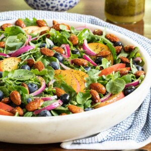 Vertical closeup photo of a Blueberry Peach Poppy Seed Salad in a white marble serving dish.