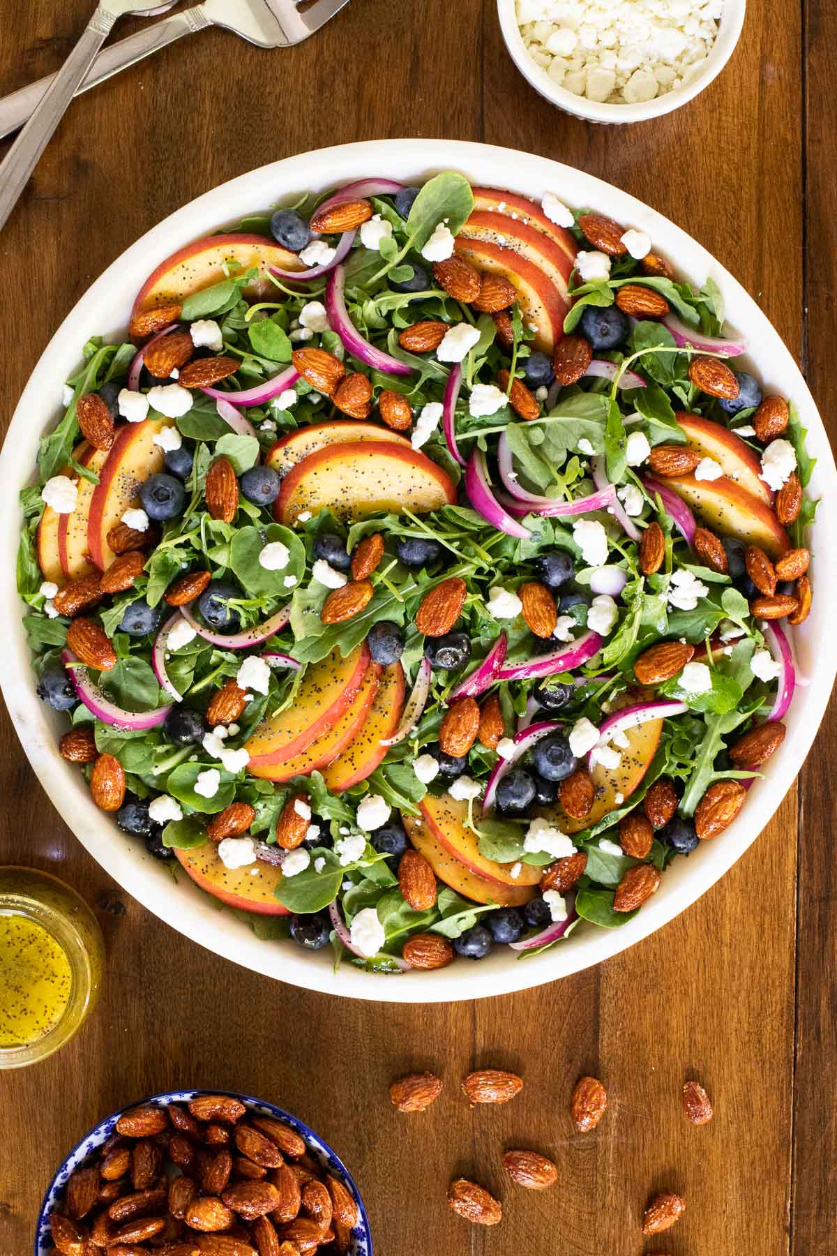 Overhead vertical photo of Blueberry Peach Poppy Seed Salad in a round white granite serving bowl on a wooden table.