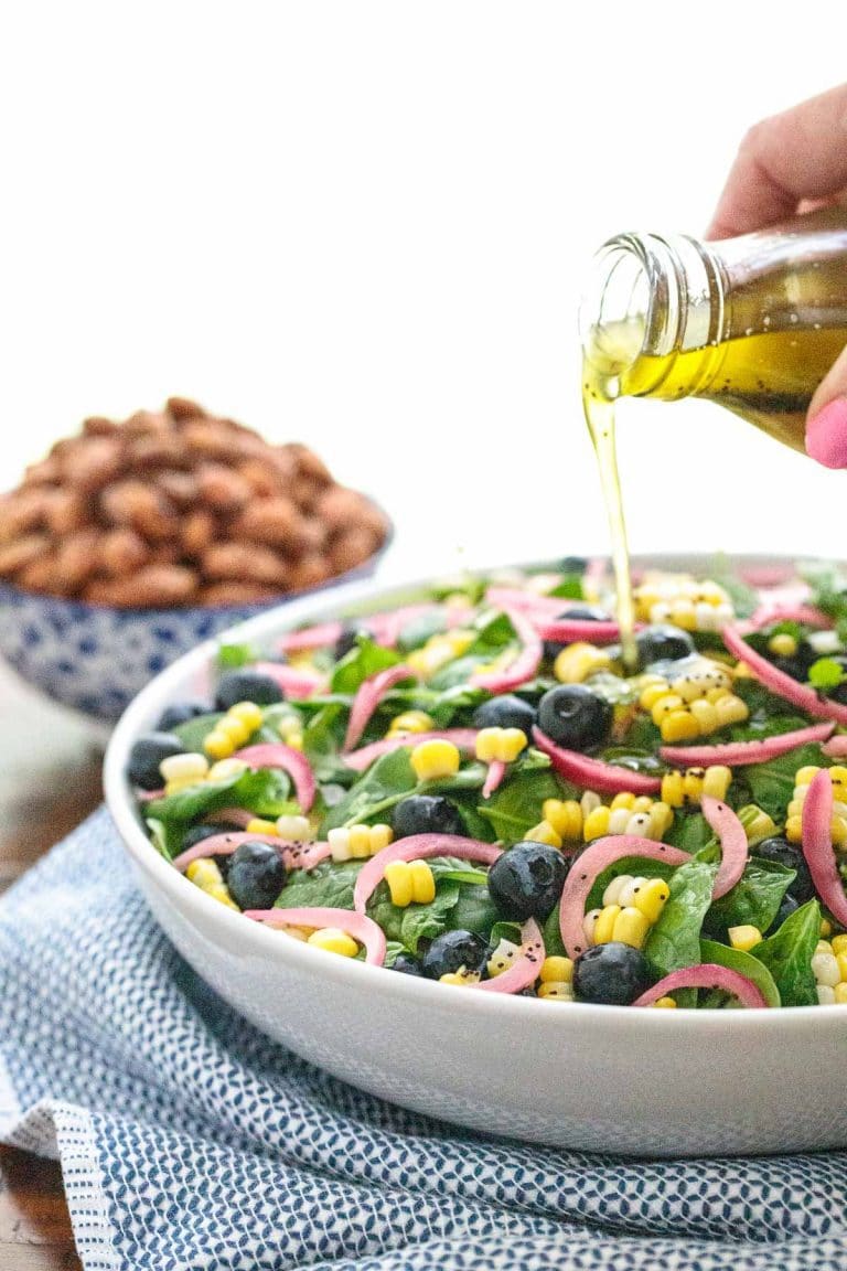 Vertical picture of Blueberry and Fresh Corn Spinach Salad in a white bowl with dressing poured from above