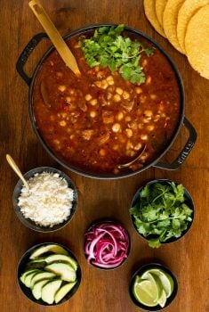Vertical overhead photo of a pot of Braised Pork Shoulder Pozole on a wood table.