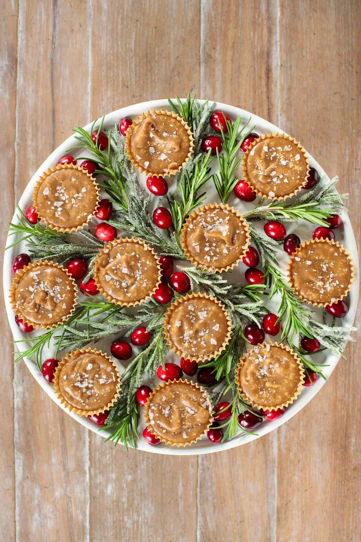 Overhead photo of a white platter filled with Sea Salted Brown Sugar Fudge surrounded by sugared rosemary branches and cranberries.