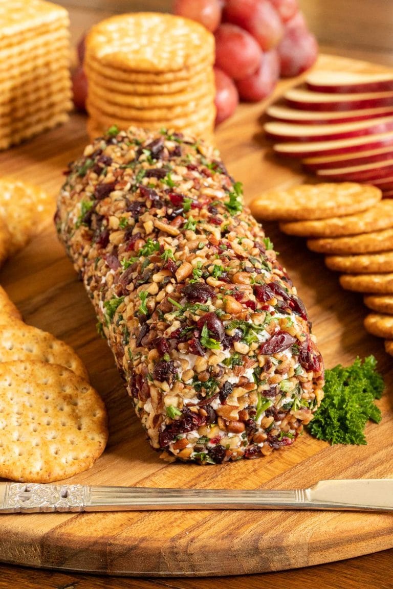 Vertical picutre of Buttered Pecan Goat Cheese Log on a wooden cutting board