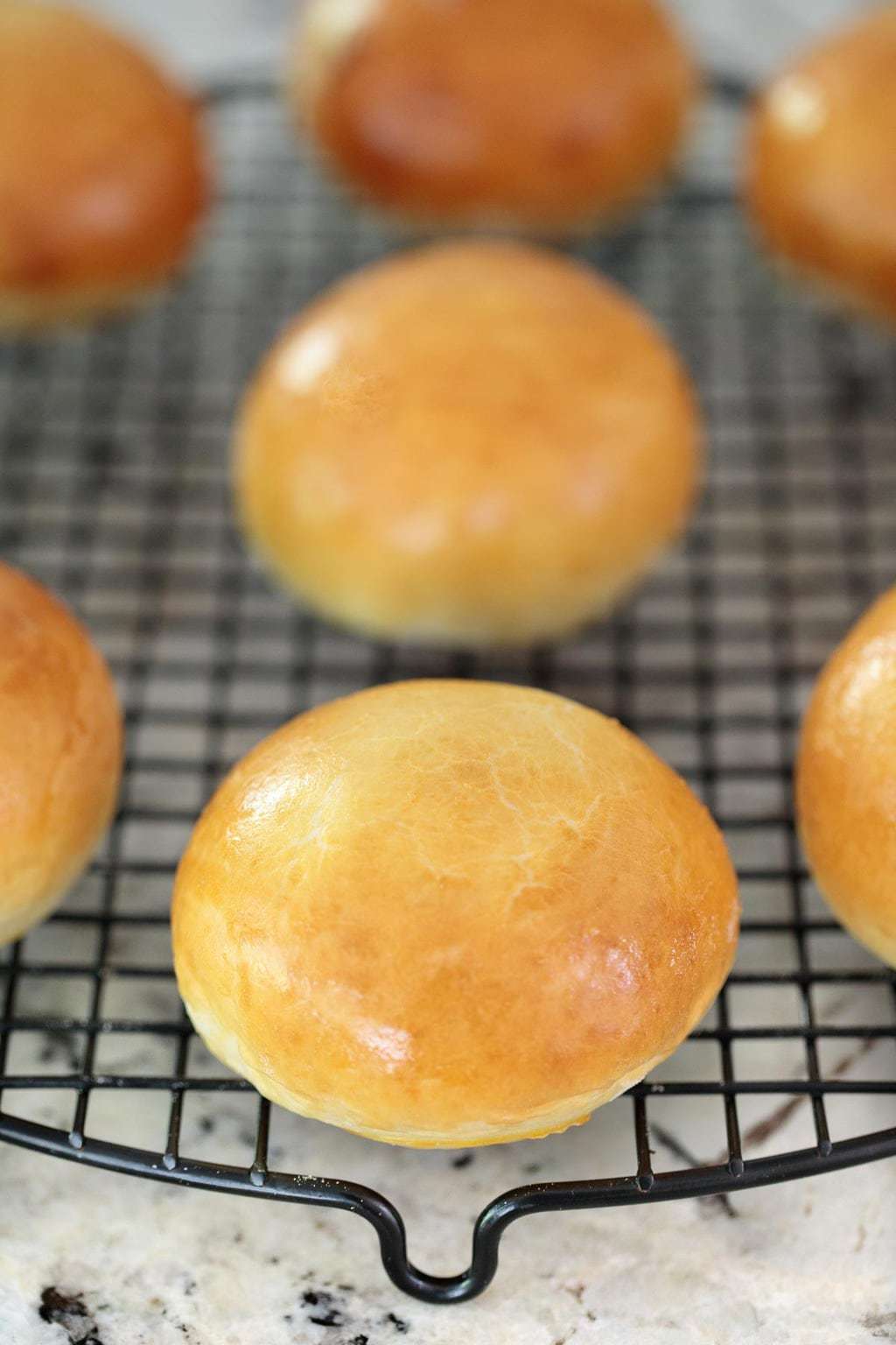 Photo of Easy Buttermilk Brioche Buns on a black cooling rack sitting on a granite countertop.