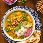 Overhead picture of Butternut Chicken Coconut Curry in a bowl garnished with toppings and naan bread