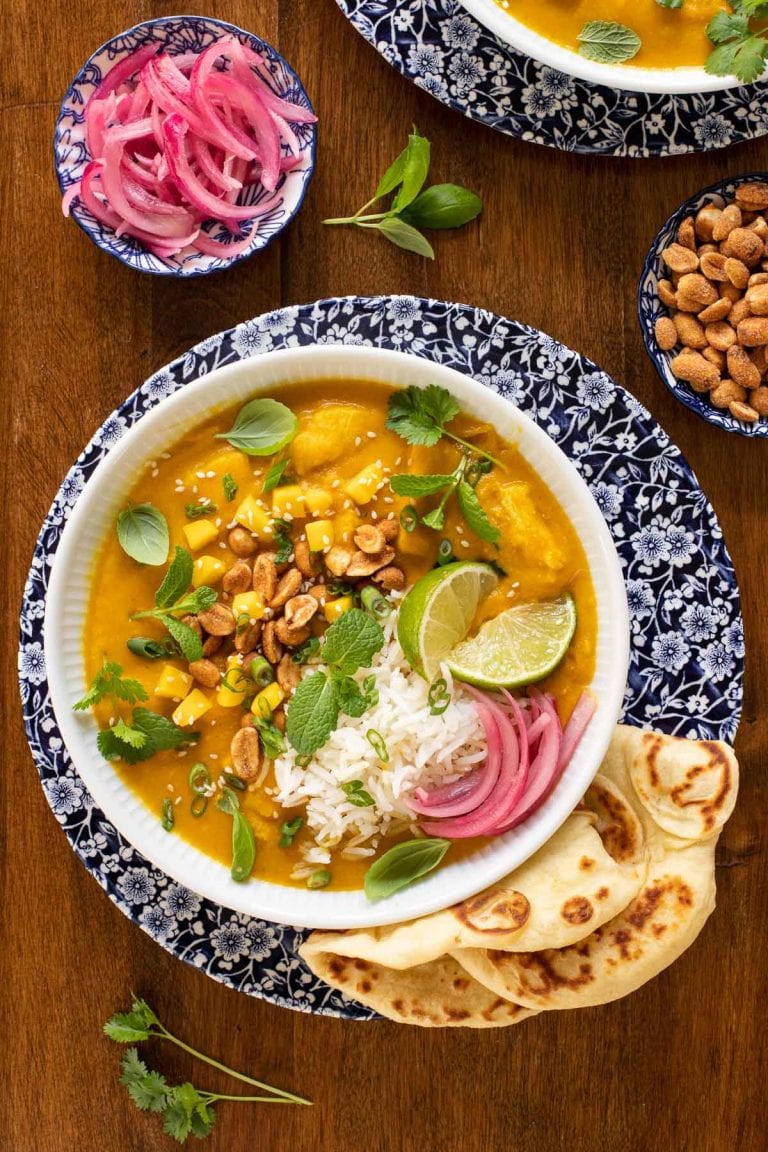 Overhead picture of Butternut Chicken Coconut Curry in a bowl garnished with toppings and naan bread