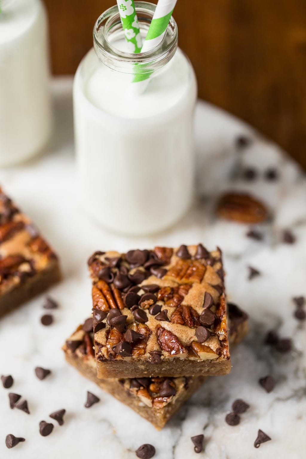 Photo of two Candied Pecan Brown Butter Blondies on a marble slab with jars of milk in the background.