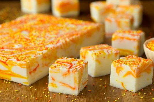 Horizontal photo of Candy Corn Swirled Fudge with a slab of fudge on the left and pieces of the fudge on the right and in the background.
