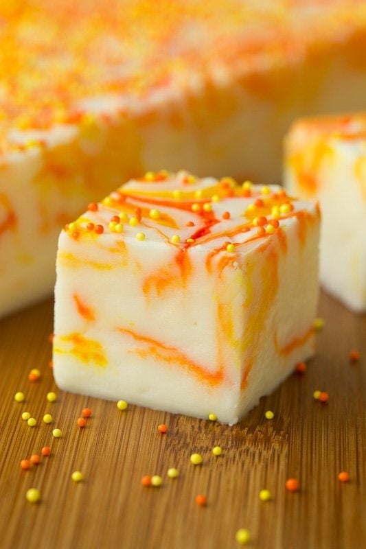 Closeup photo of a square piece of Candy Corn Swirled Fudge with a slab of the fudge in the background.