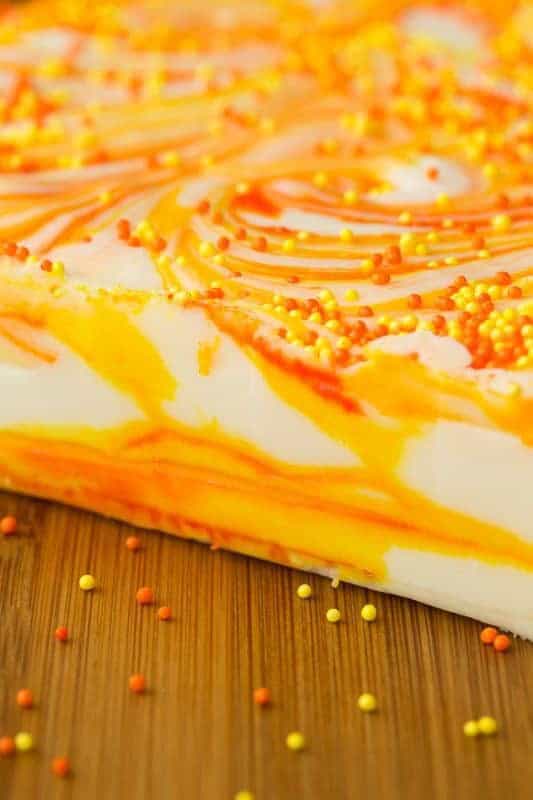 Extreme closeup of the side of a slab of Candy Corn Swirled Fudge on a wood cutting board.