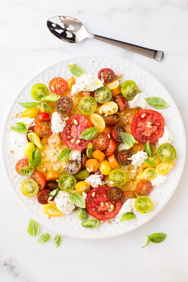 Overhead vertical photo of an Essence of Summer Caprese Salad on white serving plate on a white marble surface.