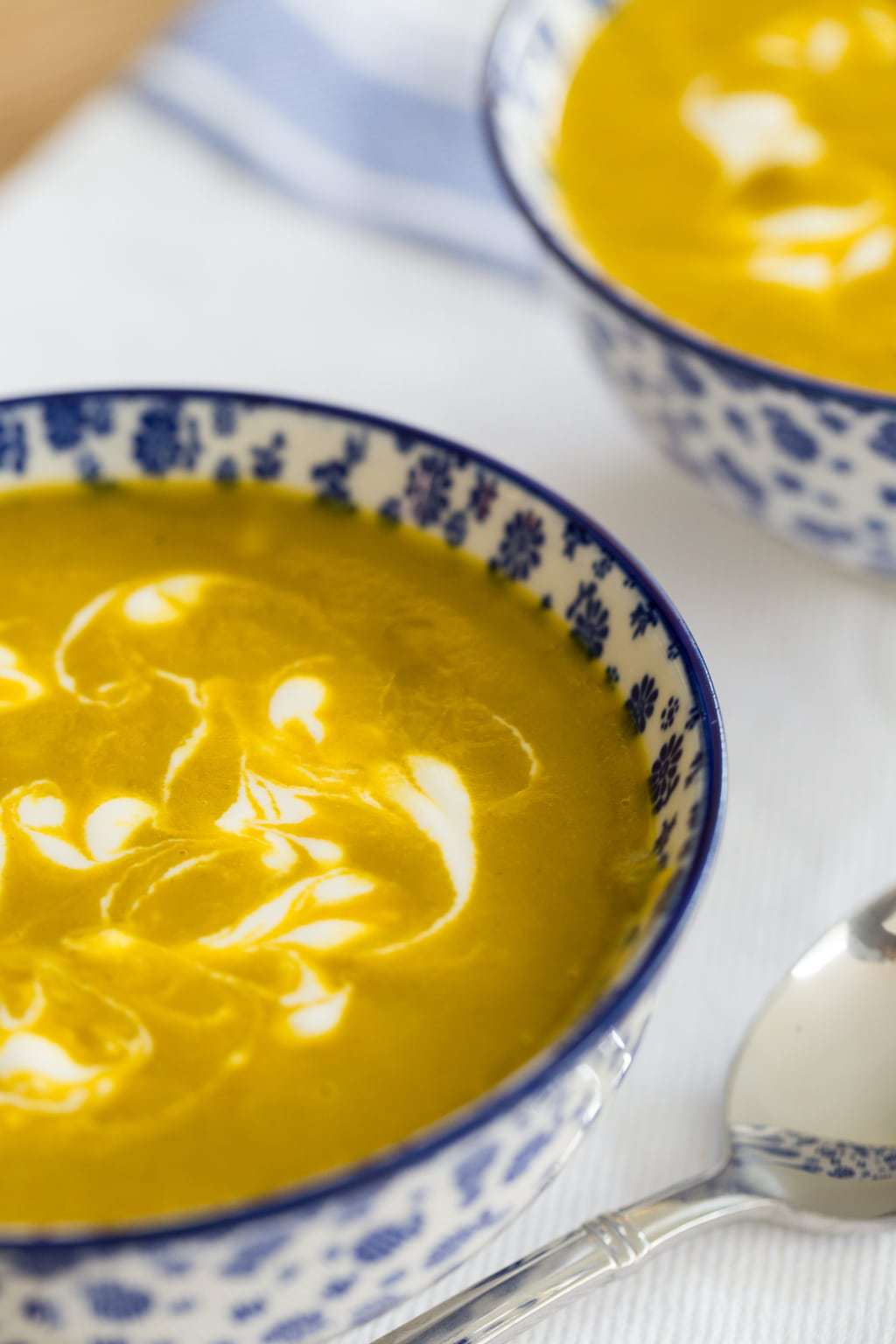 Vertical closeup photo of Carrot Coriander Soup in blue and white patterned serving bowls.