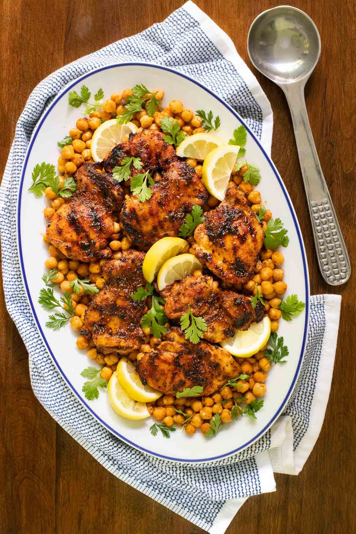 Vertical overhead photo of a blue trimmed white serving platter of Charred Honey Lemon Chicken with Crispy Chickpeas on a wood table.
