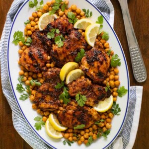 Overhead vertical photo of a presentation platter filled with Charred Honey Lemon Grilled Chicken with Crispy Chickpeas on a wood table.